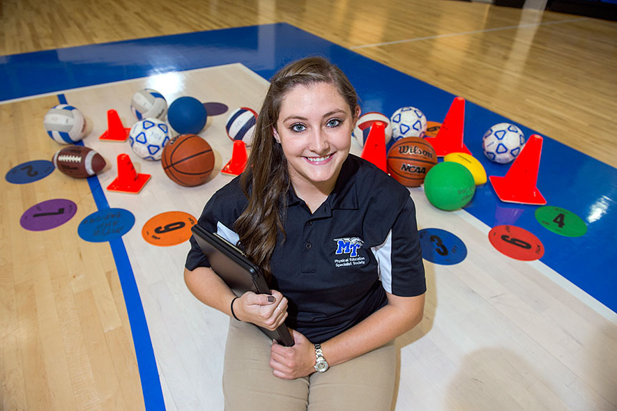 Physical education student in a gym with sports balls and equipment.
