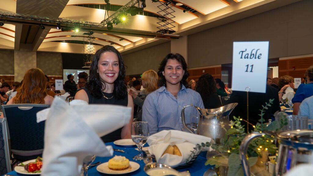 Two smiling students seated at table with place settings and centerpiece.