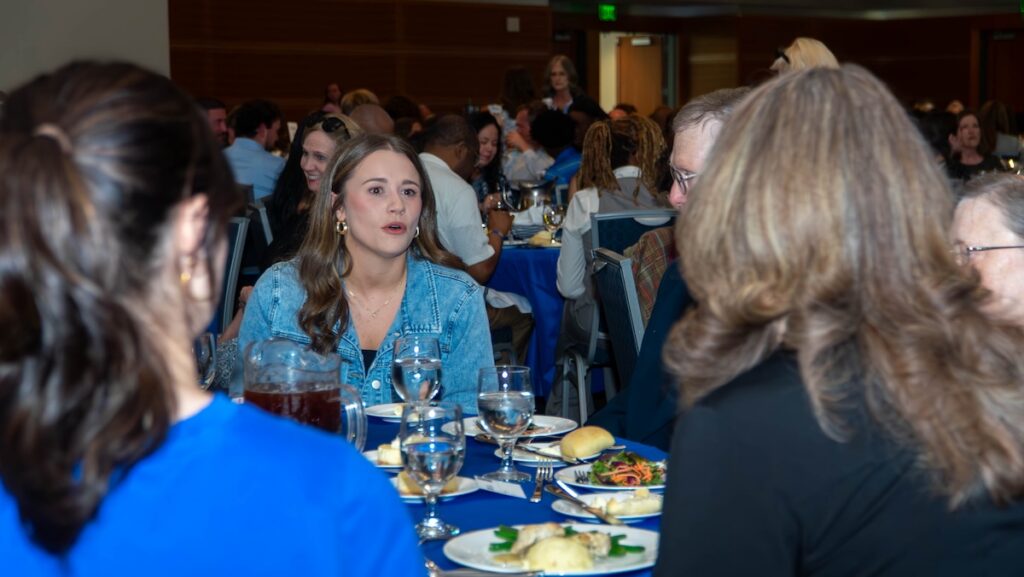 Woman in denim shirt conversing with older woman across dining table.