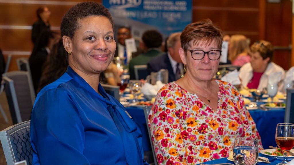 Two people smile at a dining table during the awards event, with table settings and beverages visible in the background.