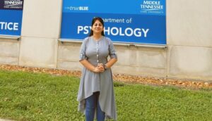 Dr. Meenakshi Shukla standing in front of the Psychology Department banner of the Academic Classroom Building at MTSU.
