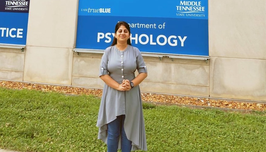 Dr. Meenakshi Shukla standing in front of the Psychology Department banner of the Academic Classroom Building at MTSU.